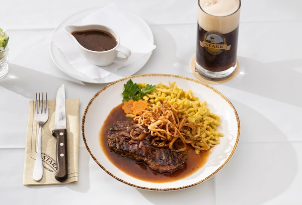 Braten mit Sp&auml;tzle und R&ouml;stzwiebeln, daneben ein dunkles Bier