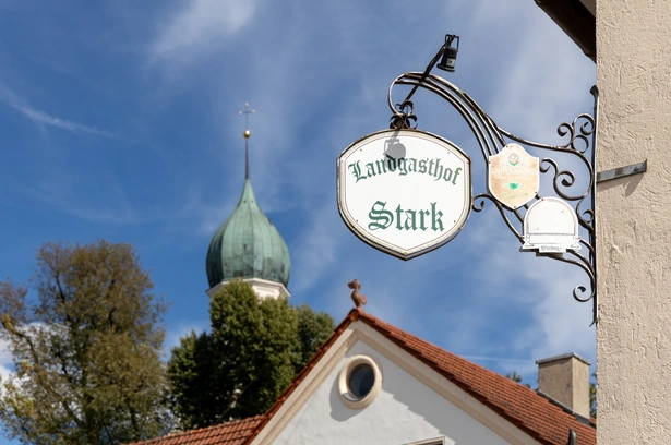 Wirtshausschild des Landgasthofs Stark vor dem Kirchturm von Gottmannshofen